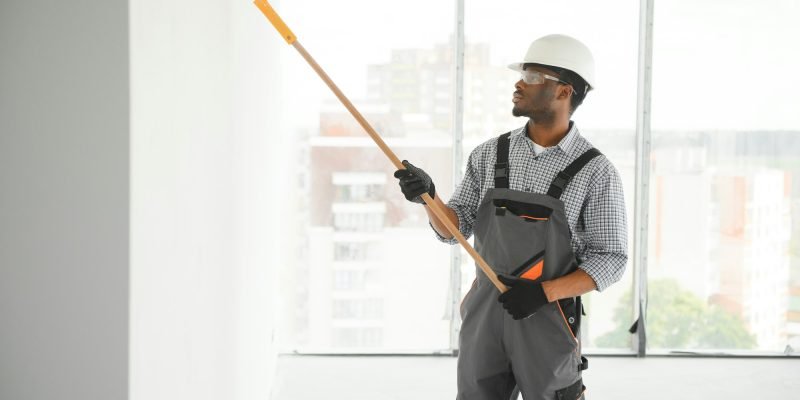 African man paints a white wall with a roller. Repair of the interior