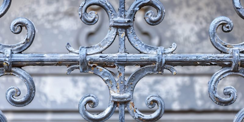 Decorative wrought iron fence with flaking paint, showing its age and weathering