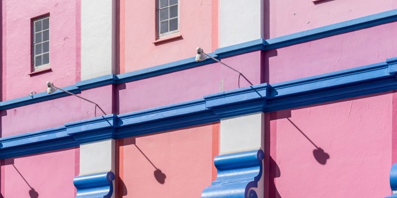 The wall of a building painted in blue, pink and purple colors under the sun light